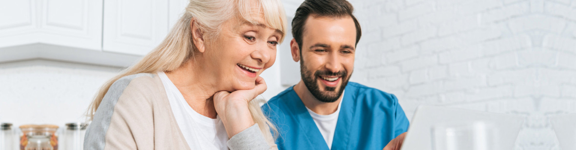 smiling young caregiver and happy senior woman using laptop together